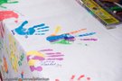 Eine weiße Tischdecke, die auf einem Tisch liegt. Auf der Tischdecke sind viele bunte Handabdrücken