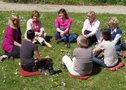 Eine Gruppe von Menschen sitzt in einem Kreis auf einer Wiese
